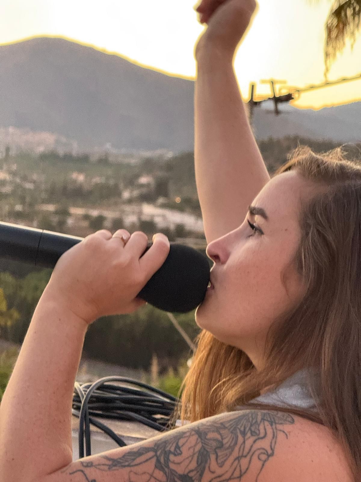 Jazmynne singing into a microphone at a sunset event