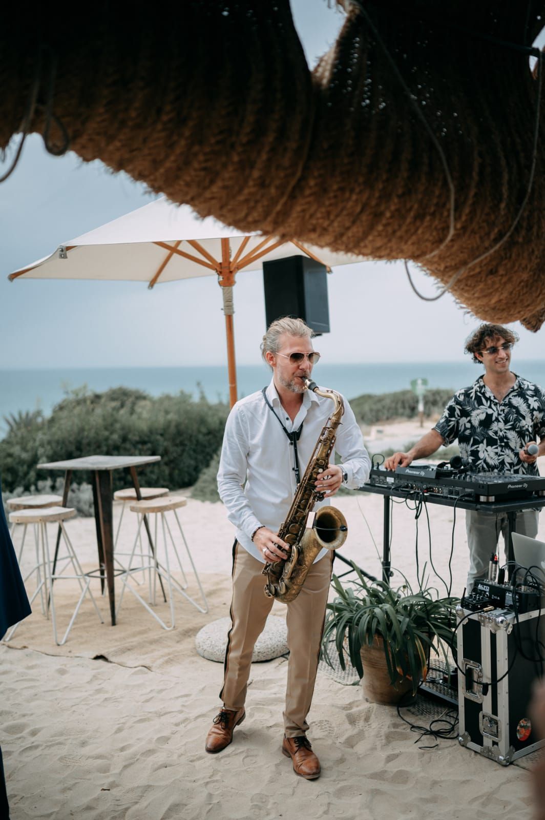 Saxophonist and DJ playing together by the sea